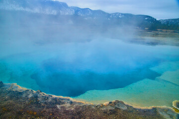 Obraz premium Huge blue pool emits sulfur steam in Yellowstone basin
