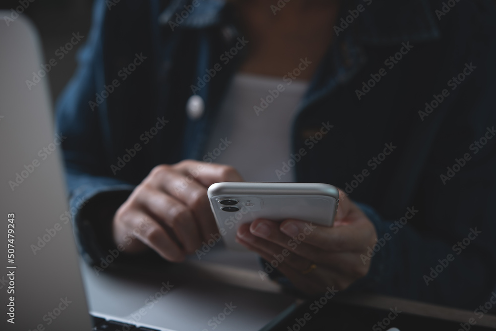 Poster closeup of business woman using mobile smart phone and working on laptop computer with digital table