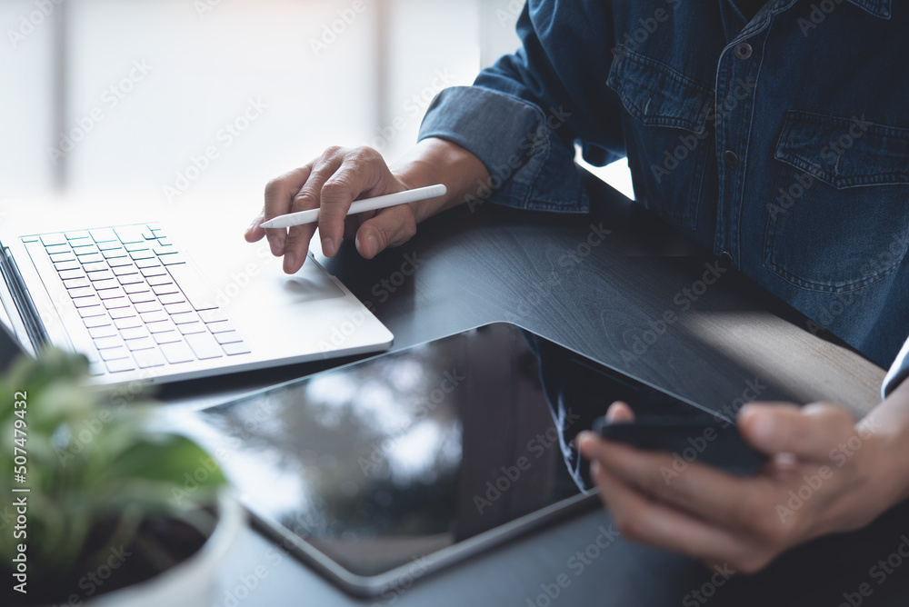Poster close up of casual business man working on laptop computer, using mobile phone and digital tablet on