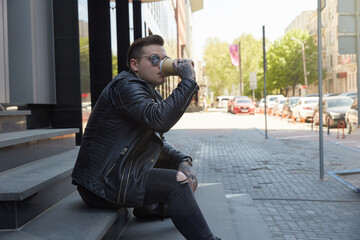 Tattooed man on the streets sitting on stairs with coffee and sunglasses 