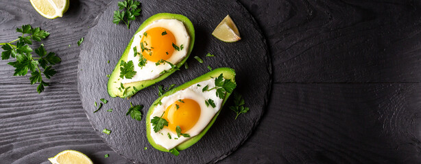 Avocado baked with eggs, fresh arugula, ground pepper on dark background, Low carb high fat breakfast. top view