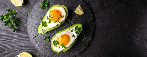 Avocado baked with eggs, fresh arugula, ground pepper on dark background, Low carb high fat...