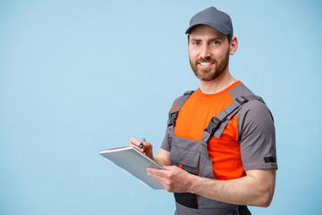Fototapeta premium Smiling Delivery man in uniform holding tablet and taking work notes