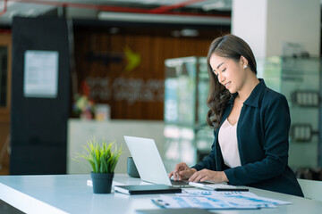 Portrait of Asian businesswoman working on her laptop computer and financial graphs in her workstation. Asian girl employee independent online marketing Ecommerce Telemarketing Ideas Report