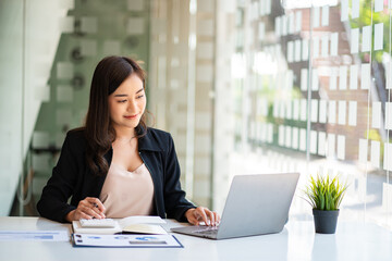 Portrait of Asian businesswoman working on her laptop computer and financial graphs in her workstation. Asian girl employee independent online marketing Ecommerce Telemarketing Ideas Report