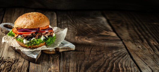 Tasty grilled homemade burgers with beef, tomato, cheese, bacon and lettuce on rustic wooden...