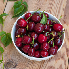 Ripe red cherries in a bowl and next to it on wooden table