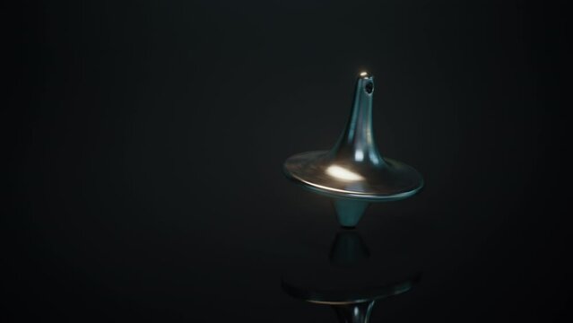 The closeup of a spinning top spins and moves towards the camera, then slows down, swings and stops. The spinning top spins on the black surface.