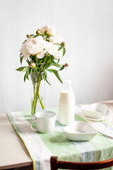 Breakfast with milk and cornflakes. white dishes and peonies on the table.
