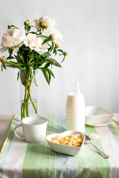 Breakfast with milk and cornflakes. white dishes and peonies on the table.