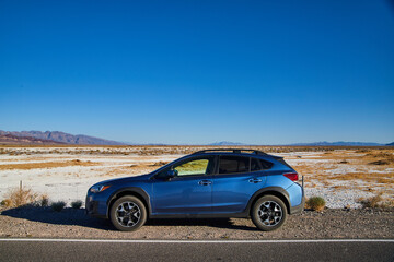 Fototapeta na wymiar Blue Subaru Crosstrek parked on road with white sand desert in background outside Death Valley