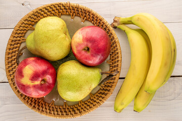 Two juicy organic pears, two red apples and a bunch of bananas with a ceramic dish on a wooden table, close-up, top view.