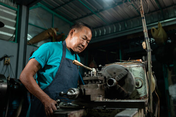 Portrait of Asian senior man working as a steel lathe is preparing work and equipment to turn steel and a small lathe in the family industry.