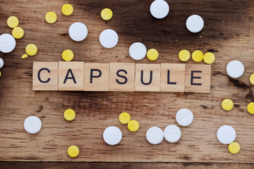 wooden block word concept with the word capsule, with a wooden background and yellow and white tablet medicine