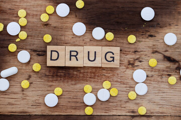 wooden block word concept with the word drug, with wooden background and yellow and white tablet medicine