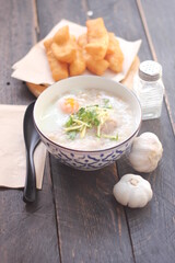 Congee in a Thai-patterned cup and fried batter served in an Asian-style cup on a black table with...