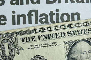 A US one dollar bill lying below a newspaper headline news on inflation. Concept for the dollar buying power amidst rising goods prices due to shortages and increasing demand. Closeup macro view. - obrazy, fototapety, plakaty