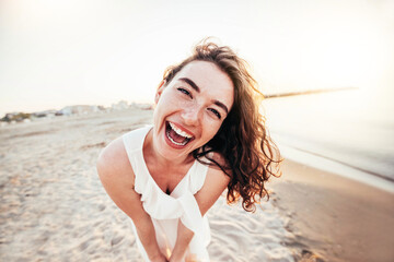 Young joyful woman in white shirt smiling at camera on the beach - Traveler girl enjoying freedom...