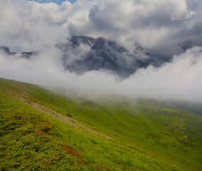 Fototapeta na wymiar green mountain slope in dense mist and clouds, natural travel background