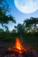 huge moon shining above campfire in forest , natural camping twilight background