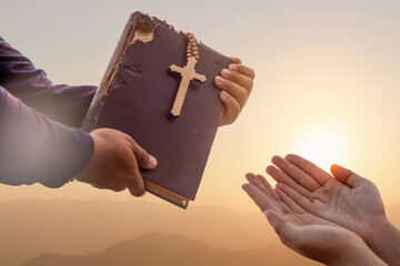 Close up father hand giving Bible and Cross legacy to young person at sunset background, Religion...