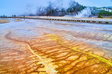 Colorful waves by boardwalk in Yellowstone with steam covering mountains