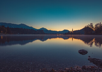 Lake Bled at Sunrise. Church, castle and the mountains are basking in the morning sun