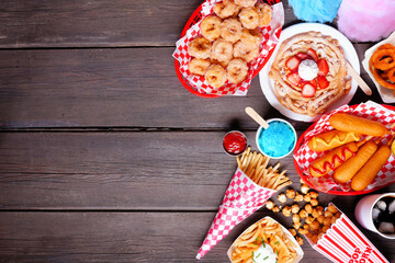 Carnival theme food side border over a dark wood background. Top view with copy space. Summer fair concept. Corn dogs, funnel cake, cotton candy and snacks. - obrazy, fototapety, plakaty