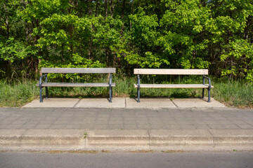 Two empty roadside benches in front of green bushes implying a solitude