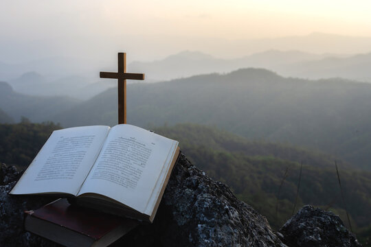 Bible and crucifix symbol on top mountain with bright sunbeam on the colorful sky background