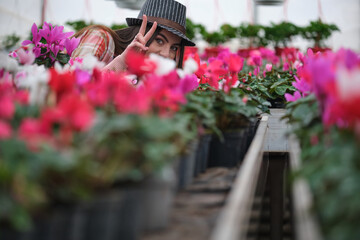 Fototapeta na wymiar Funny young girl in hat standing between pink cyclamen flowers with notebook in greenhouse. White and pink colors. Selecvtive focus