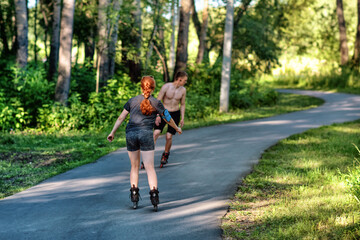 A sporting girl and a boy roller skating in a park on summer day.