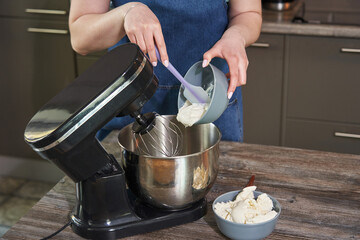 female hands puts the ingredients into a large culinary mixer for whipping and stirring