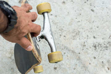 Man holds used skateboard in his left hand on a concrete background © DAVISUALS