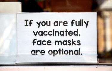 Covid related sign in a store window stating  face masks are optional if a person is vaccinated