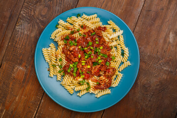 Blue plate with bolognese pasta on a wooden table sprinkled with onions.