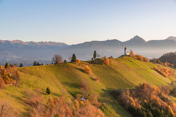 Church on the hill at sunrise. Beautiful scenery at Jamnik, Slovenia. Panoramic view of the mountains behind the church in the early morning. - obrazy, fototapety, plakaty