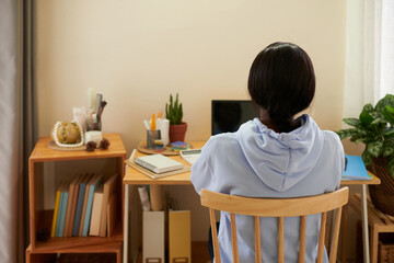 High school student studying at home for upcoming class, view from back