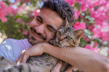 close up. Young man hugs a gray tabby cat with green eyes in the garden and smiles