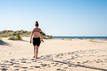 Rear view of a woman walking on the fine sand of the beach at sunset.