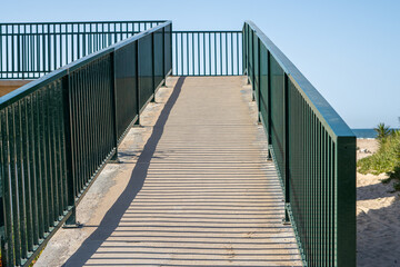 Wheelchair-enabled walkway, with metal railing, on a beach at sunset.