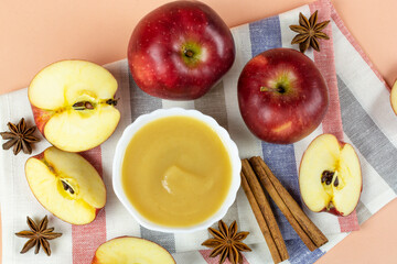 Applesauce in a white bowl with a spoon, red ripe apples and cinnamon sticks. Healthy lifestyle, sauce, mousse, baby food, ingredients.