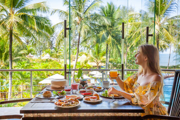 Tropical vacation. Breakfast in modern hotel resort with sea and palm trees on background. Traveler woman on summer holidays on Phuket, Thailand. Exotic travel in Southeast Asia