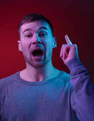 Caucasian man's portrait isolated on dark red studio background in neon, multicoloured. Emotion of remembrance with open eyes and a raised finger. Concept of human emotions, facial expression, sales, 