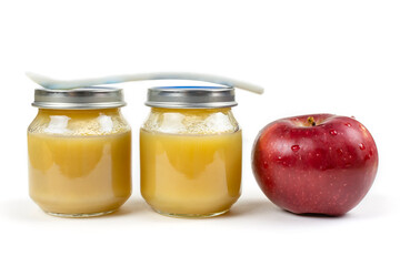 Two glass jars with baby apple puree with a spoon and a red ripe apple on a white isolated background. The first fruit lure of the baby. Nutrition of the child.