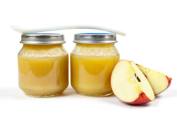 Baby food. Two glass jars with baby apple puree with a spoon and slices of red ripe apple on a white isolated background. The first fruit lure of the baby.