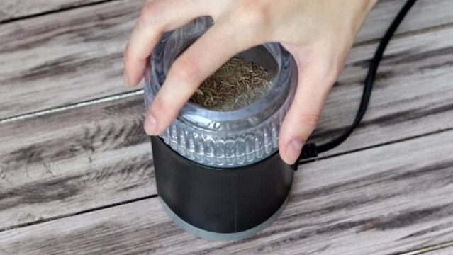 Turning zira into powder in a coffee grinder. A woman's hand grinds cumin spice.