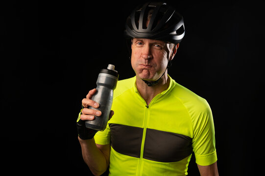 Cyclist in a yellow jersey drinking from a water bottle on a black background with copy space