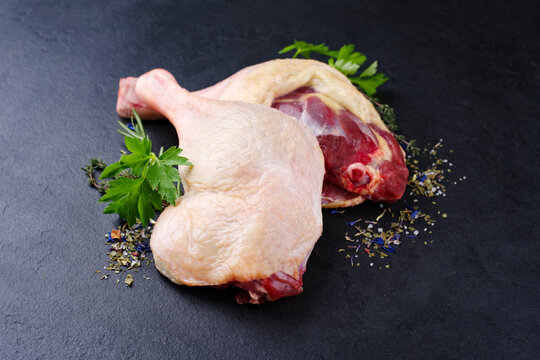 Traditionelle rohe Gourmet Entenkeule mit Kr&auml;utern und Gew&uuml;rzen angeboten als close-up auf einem schwarzen Design Board 