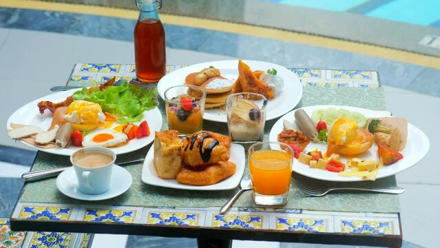 Breakfast at luxury hotel by the pool. Table with delicious food by the poolside, travel in resort on sunny summer day. Rest and vacation in luxury modern hotel. Buffet food